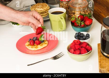 Mann beim Frühstück mit einer Tasse Kaffee und Pfannkuchen mit Beeren Stockfoto