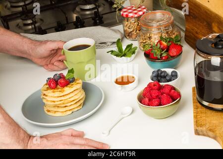 Mann beim Frühstück mit einer Tasse Kaffee und Pfannkuchen mit Beeren Stockfoto