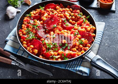 Nahaufnahme der Kichererbsen fritos, heiße Kichererbsen Eintopf mit Chorizo in Scheiben, Schinken, Tomaten und Gewürzen in einer Pfanne auf einer konkreten Tabelle mit Zutaten, Spani Stockfoto