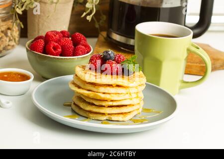 Pfannkuchen mit Beeren und Honig auf einem grauen Teller und mit einer Tasse Kaffee auf einer Küchentheke Stockfoto