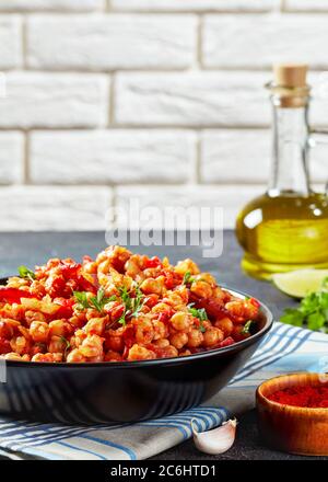 Garbanzos fritos, heißer Chickpea Eintopf mit Chorizo, Tomaten und Gewürzen in einer schwarzen Schüssel auf einem Betontisch mit Zutaten auf dem Hintergrund von Ziegel Stockfoto