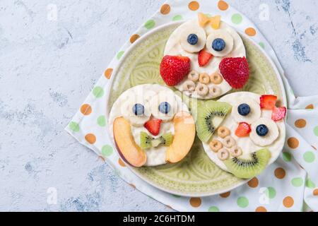 Reiskuchen mit Joghurt und frisches Obst in Form von niedlichen Eulen auf einem Teller, Mahlzeit für Kinder Idee, Draufsicht Stockfoto