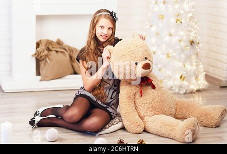 Junge süße Teenager-Mädchen umarmt einen großen weichen Teddybär im Inneren mit Weihnachtsdekorationen Stockfoto