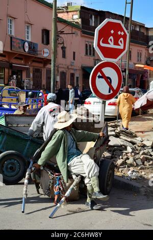 Marrakesch, Marokko - 23. November 2014: Unbekannte Menschen auf einer Straße mit Verkehrsschildern und Schubkarren Stockfoto