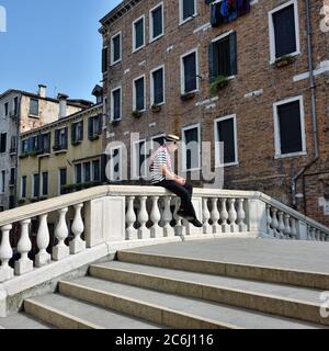 VENEDIG, ITALIEN - 27. SEPTEMBER 2014: Ein nicht identifizierter Mann in Gondolierkleidung sitzt am Brückenzaun in Venedig. Gondeln Reise ist die beliebteste touristische Eingabe Stockfoto