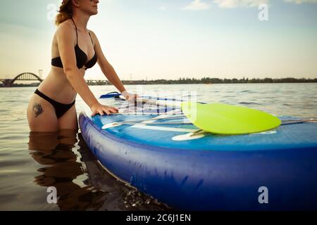 Zeit zum Genießen. Junge attraktive Frau trägt Paddle Board, SUP. Aktives Leben, Sport, Freizeitangebot. Kaukasische Frau auf Reise Bord im Sommer Abendzeit. Urlaub, Resort, Genuss. Stockfoto