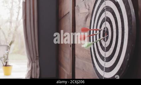 Drei Darts Pfeile treffen das Bullseye. Dartscheibe, die an einer Holzwand von zu Hause oder im Büro hängt. Ziel- oder Zielkonzept erreichen. Nahaufnahme. Getöntes Bild Stockfoto