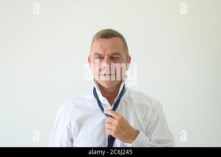 Mann mittleren Alters winkend, als er seine Krawatte mit der Hand in einem frontalen Porträt auf weißem Hintergrund löst Stockfoto
