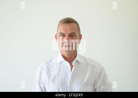 Ernsthafter Mann mittleren Alters in einem schicken weißen Hemd starrt in einem frontalen Kopf- und Schulterportrait auf Weiß aufmerksam auf die Kamera Stockfoto