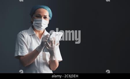 Ärztin nutzt digitale Tablette. Frau im medizinischen Mantel steht auf grauem Hintergrund. Moderne Technologie und Gesundheitskonzept. Leer für Banner mit Stockfoto