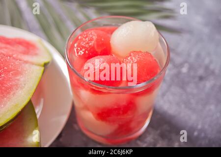 Tropischer Obstsalat mit Melone und Wassermelonenbällchen im Glas unter dem Palmblatt. Stockfoto