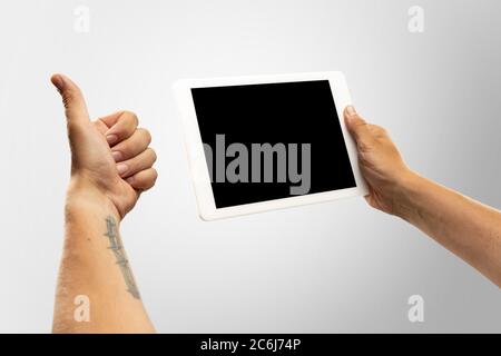 Daumen hoch, nett, entzückt. Nahaufnahme männliche Hände halten Tablet mit leerem Bildschirm während Online-Wiedergabe von beliebten Sportspielen, Meisterschaften. Copyspace für Werbung. Geräte, Gadgets, Technologien Konzept. Stockfoto