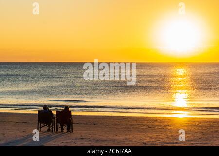 Zwei Leute sitzen am Strand und genießen den Sonnenuntergang Stockfoto
