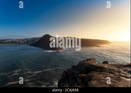 Blick auf die Landzungen am Eingang der Bucht São Martinho do Porto, mit dem Leuchtturm, bei Sonnenuntergang. Stockfoto