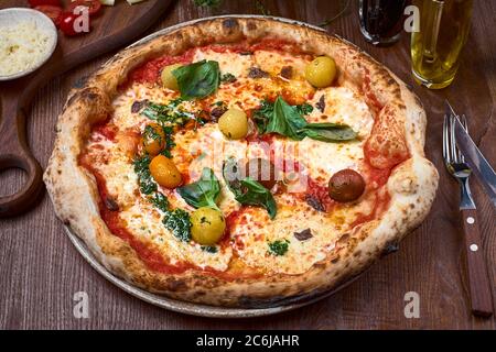 Pizza Napoli, Klassische italienische Pizza mit Tomatensauce, Mozzarella-Käse, Sardellen und Basilikum auf dunklem Holztisch. Stockfoto