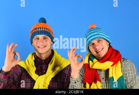 Zwillingsbrüder tragen warme Hüte und Schals und zeigen gute Schilder. Geschwister genießen die Herbstzeit. Männer mit fröhlichen Gesichtern auf blauem Hintergrund. Herbst-Verkauf und warme Saison Konzept. Stockfoto