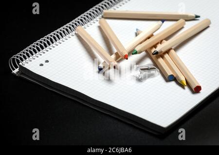 Flache Ansicht von weißem Notizbuch, Farbstifte und Bleistiftspitzer auf einem Tisch. Vorbereitung auf eine Schule. Zurück zur Schule. Stockfoto