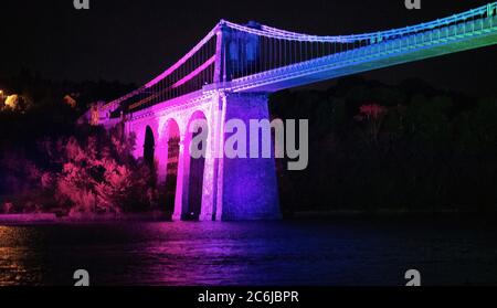 Bangor, Gwynedd, N Wales. Die Menai-Hängebrücke über die Menai-Straße wird in Regenbogenfarben beleuchtet, um 72 Jahre NHS zu feiern Stockfoto