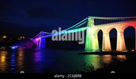 Bangor, Gwynedd, N Wales. Die Menai-Hängebrücke über die Menai-Straße wird in Regenbogenfarben beleuchtet, um 72 Jahre NHS zu feiern Stockfoto