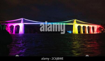 Bangor, Gwynedd, N Wales. Die Menai-Hängebrücke über die Menai-Straße wird in Regenbogenfarben beleuchtet, um 72 Jahre NHS zu feiern Stockfoto