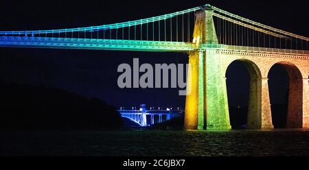 Bangor, Gwynedd, N Wales. Die Menai-Hängebrücke über die Menai-Straße wird in Regenbogenfarben beleuchtet, um 72 Jahre NHS zu feiern Stockfoto