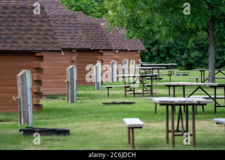 Reihen von rustikalen Campinghütten, mit Wasserpumpen und Picknicktischen auf einem Campingplatz Stockfoto