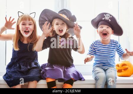 Fröhlicher Bruder und zwei Schwestern an Halloween. Lustige Kinder in Karnevalskostümen drinnen. Fröhliche Kinder spielen auf dem Fenster sitzen. Stockfoto