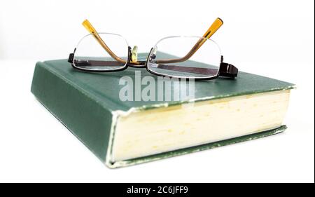 Gebrauchte Gläser auf dem grünen alten Buch. Lesebrille und Vintage-Buch isoliert auf weißem Hintergrund Stockfoto