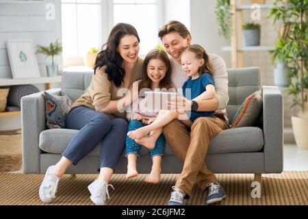 Glückliche liebevolle Familie. Junge Mutter, Vater und ihre Töchter Mädchen spielen zu Hause. Lustige Mama, Papa und schöne Kinder haben Spaß mit Tablet. Stockfoto