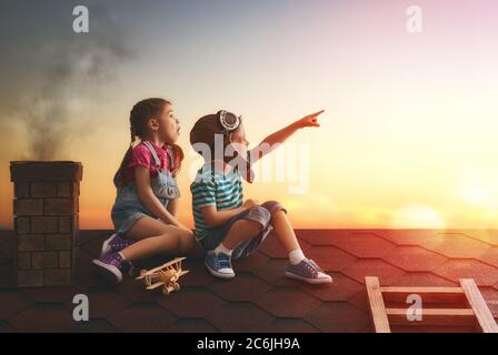 Zwei kleine Kinder spielen auf dem Dach des Hauses und schauen in den Himmel und träumen davon, Pilot zu werden. Stockfoto