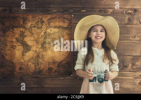 Gehen Sie auf ein Abenteuer! Nettes Kind Mädchen mit Vintage-Kamera auf Holz Hintergrund Wand und Karten. Stockfoto