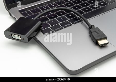 Detaillierte Abbildung eines HDMI-Videoadapters, der auf der Tastatur eines geöffneten, bekannten Notebook-Computers aufliegt. Stockfoto