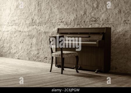 Altes Klavier in einem alten Raum mit Steinwänden und Holzboden mit sanftem Licht aus einem Fenster. Stockfoto