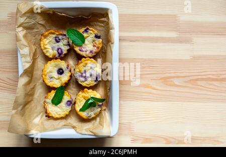 Hausgemachte Hüttenkäse-Muffins mit Heidelbeeren in einem Gericht auf einem natürlichen Holzhintergrund. Flach legen, kopieren Raum Stockfoto