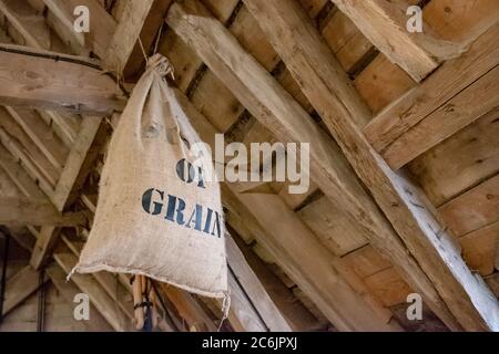 Detaillierte Abbildung eines Stoffsacks voller geerntetem Getreide, das in einem großen Stalldach hängend zu sehen ist. Der Hintergrund zeigt die vielen verwendeten Hölzer. Stockfoto