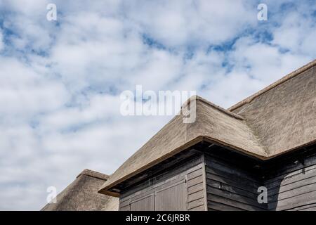 Außenansicht eines großen, holzbebauten Land- und Lagergebäudes mit seinem renovierten Strohdach. Die Eingangstüren sind geschlossen zu sehen. Stockfoto