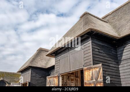 Außenansicht eines großen, holzbebauten Land- und Lagergebäudes mit seinem renovierten Strohdach. Die Eingangstüren sind geschlossen zu sehen. Stockfoto