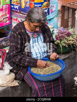 Guatemala, Solola Department, Santiago Atitlan, EINE Maya-Frau in traditionellen Kleid sortiert Nüsse zum Verkauf auf dem Markt. Stockfoto