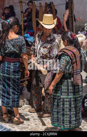 Guatemala, El Quiche Department, Chichicastenango, EIN Maya-Mann in der unverwechselbaren Outfit von Solola auf dem indischen Markt, einschließlich einer schweren Wolle Rodillera um seine Taille. Er kauft einen neuen Holzgriff für seine Ackerbauschanze. Mit ihm sind seine Frau und Tochter in traditioneller Kleidung. Stockfoto