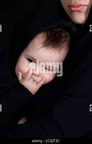 Niedliches Baby-Portrait mit Heavy Metal und Hard Rock Symbol - Hornhand auf schwarzem Hintergrund. Mutter hält ihr Kind Stockfoto