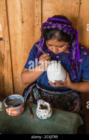 Guatemala, Solola, San Antonio Palopo, EINE junge Maya-Frau, die in typischen traditionellen Kleidern in einer Werkstatt Entwürfe auf Keramik malt. Stockfoto