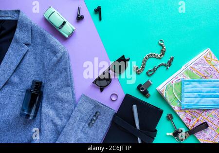 Accessoires für Herren, Geräte und medizinische Schutzmaske auf lila und türkisfarbenem Hintergrund. Konzept der Annullierung Reise und Urlaub, COVID-19 pandem Stockfoto
