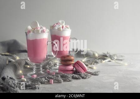 Heiße Schokolade in Rosa mit Schlagsahne und Marshmallow-Süßigkeiten in 2 Glaskrügen, süßen Pastellmakronen und Lichtern. Platz für Text kopieren. Horizont Stockfoto