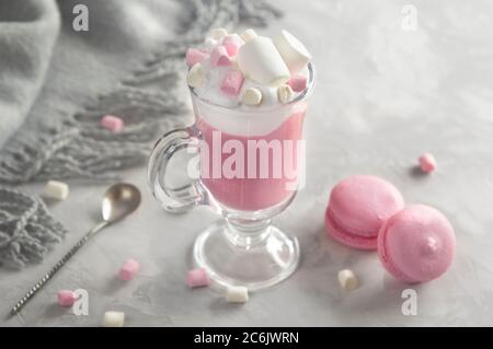 Heiße Schokolade in Rosa mit Schlagsahne und Marshmallow-Süßigkeiten in einem Glaskrug, süße Pastell-makronen auf grauem Hintergrund. Stockfoto