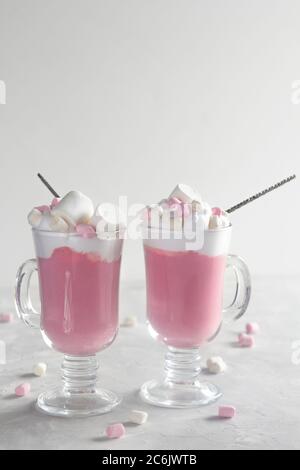 Heiße Schokolade in Rosa mit Schlagsahne und Marshmallow-Süßigkeiten in 2 Glaskrügen auf grauem Hintergrund. Speicherplatz kopieren Stockfoto