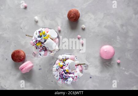 Heiße Schokolade in Rosa mit Schlagsahne und Marshmallow-Süßigkeiten in 2 Glaskrügen, süße Pastell-makronen auf grauem Hintergrund. Draufsicht Stockfoto