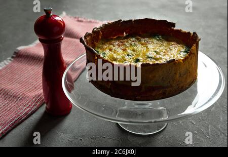 Hausgemachte französische Torte oder Quiche lorraine Lachs Pie auf einer Glasplatte serviert, rote Holzmühle Cruet Pfeffer Stockfoto
