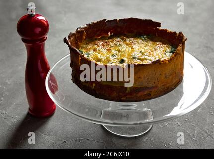 Hausgemachte französische Torte oder Quiche lorraine Lachs Pie auf einer Glasplatte serviert, rote Holzmühle Cruet Pfeffer Stockfoto