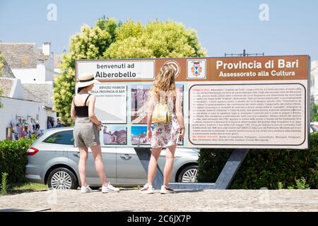 Apulien, Süditalien - Alberobello, zwei junge Mädchen vor dem Eingangsschild Besuch der UNESCO-Stadt Trulli. Stockfoto