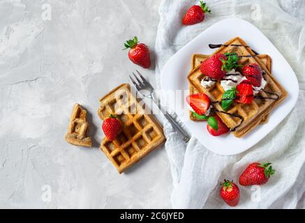 Hausgemachte quadratische belgische Waffeln mit Erdbeeren, Ricotta-Käse und Schokolade auf weißem Teller. Flach liegend. Stockfoto